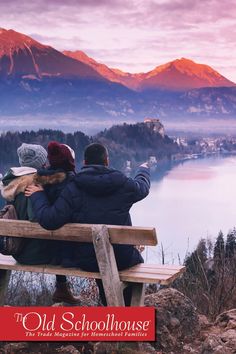 two people sitting on a bench looking out over the water and mountains in the background