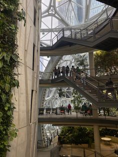 people are walking up and down the stairs in an indoor building with plants growing on it