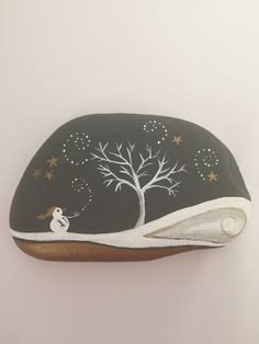 a painted rock with a tree and snowman in the night sky, on a white background