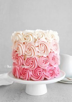 a cake with pink and white frosting on a plate next to a coffee cup