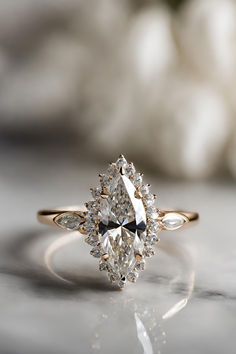 a close up of a diamond ring on a marble surface with white flowers in the background