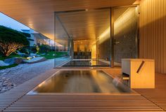 an indoor swimming pool in the middle of a wooden floored area with glass walls