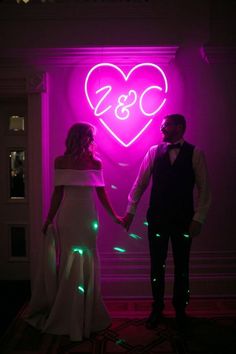 a bride and groom holding hands in front of a neon heart