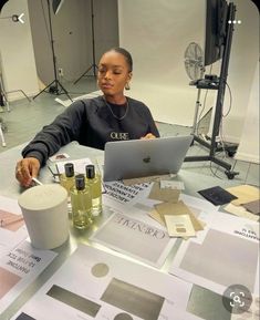 a woman sitting at a table with a laptop computer and other items on the table