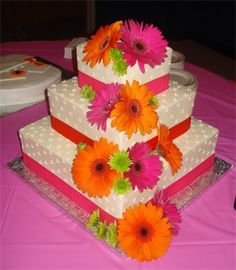 a three tiered cake with flowers on the top and bottom is white, pink, orange and green