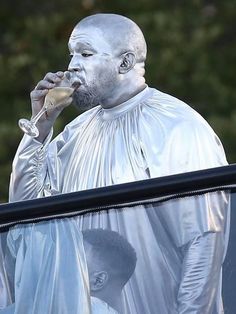 a man dressed in silver drinking from a wine glass while standing next to a window