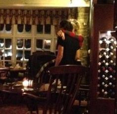 two people standing in a room with wine bottles on the wall