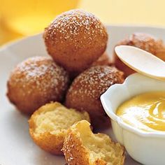 a white plate topped with donuts and dipping sauce next to some breaded pastries