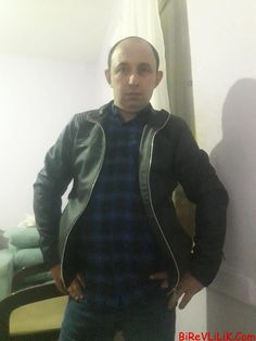 a man standing in front of a mirror wearing a black jacket and blue plaid shirt