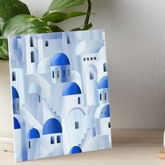 a blue and white painting on a table next to a potted plant art board print