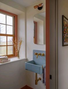 a blue sink sitting under a bathroom window next to a mirror and vase with flowers