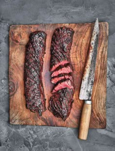 two steaks are on a cutting board with a knife and fork next to it