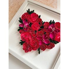 paper flowers arranged in the shape of a heart on a white frame with pink and red petals