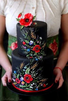 a woman holding a black cake with red flowers on it