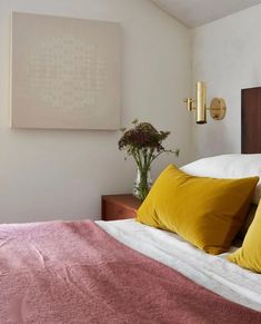 a bed with yellow and red pillows in a bedroom next to a painting on the wall