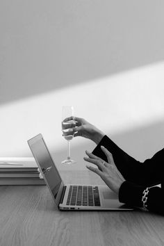 a woman sitting at a table with a glass of wine in front of her laptop