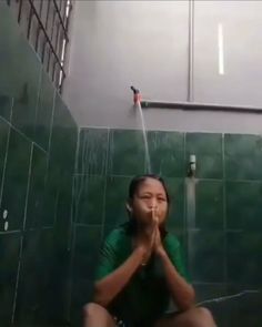 a woman sitting on the ground in front of a shower head with her hands together