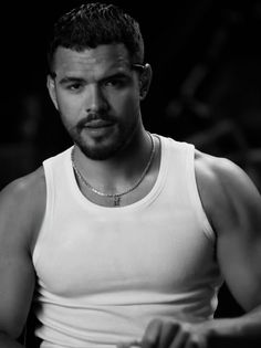 a man in white tank top sitting down with his hands on his hips and looking at the camera