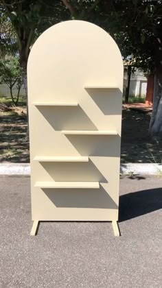 a white book shelf sitting in the middle of a parking lot next to a tree