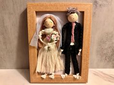 a wooden frame with two dolls dressed in wedding attire, one holding a bouquet and the other wearing a veil