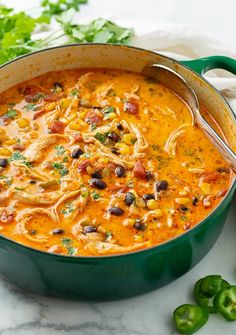 a green pot filled with chicken and bean soup next to some cilantro peppers