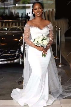 a woman in a white wedding dress standing next to a car and smiling at the camera