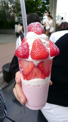 a person holding up a cup filled with ice cream and strawberries