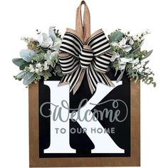 a wooden sign that says welcome to our home with a bow on it and flowers around the letter k