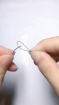 two hands are doing something with yarn on the end of a string that is being held by one hand