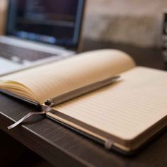 an open notebook sitting on top of a wooden desk next to a laptop and coffee cup