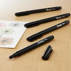 four pens are sitting on a table next to a piece of paper and some ink