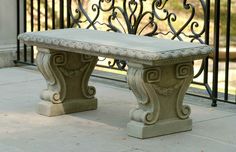 a stone bench sitting on top of a sidewalk next to a metal fence and gate