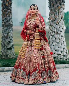 a woman in a red and gold bridal gown standing next to two palm trees