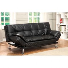 a black leather sofa sitting on top of a hard wood floor next to a window