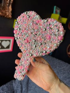 a person holding a heart shaped brooch in their left hand with beads on it