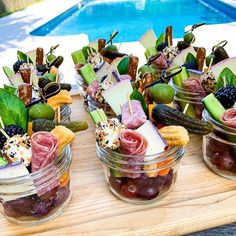 small jars filled with food sitting on top of a wooden table next to a swimming pool