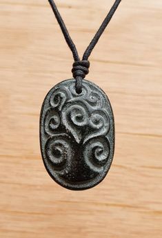 a black pendant with an intricate design on it sitting on a wooden surface next to a string