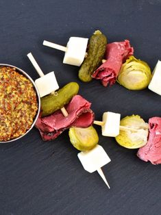 an assortment of food on skewers with pickles, cheese and sauces