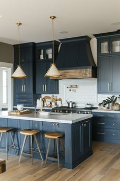 a large kitchen with blue cabinets and wooden stools in the center, along with two pendant lights hanging from the ceiling