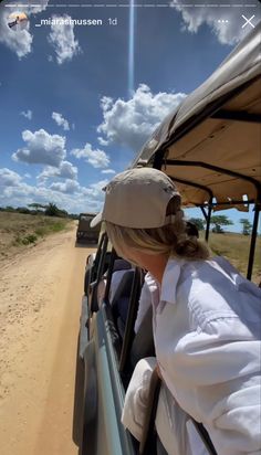 a woman sitting in the back of a vehicle on top of a dirt road next to a field