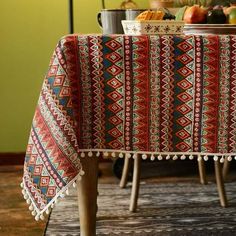 a table topped with a red and blue blanket next to a bowl of fruit on top of a wooden table