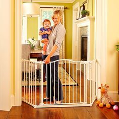 a woman holding a baby in her arms standing next to a white gate that is open