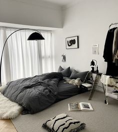 a bedroom with an unmade bed, black and white rugs, hanging clothes