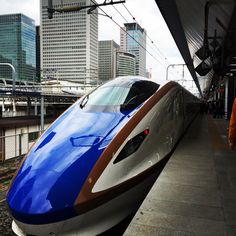 a blue and white train pulling into a station with tall buildings in the back ground