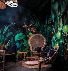 a room filled with lots of green plants and wicker furniture in front of a black wall