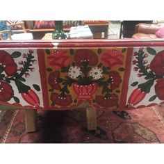 an ornately decorated table with red flowers and leaves painted on the top, in a living room