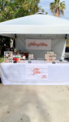 a table with some food on it under a white tent and palm trees in the background