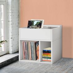 a white shelf with books and magazines on it in front of a pink painted wall