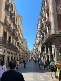 people are walking down the street in an old city with tall buildings and balconies