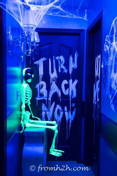 a room with neon blue walls and ghost decorations on the door, in front of an open doorway that says turn back now